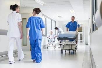 Busy hospital hallway, with a doctor and nurses walking.