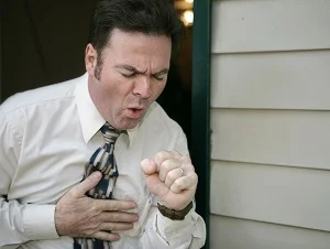 A person, wearing a white shirt and tie, coughing.