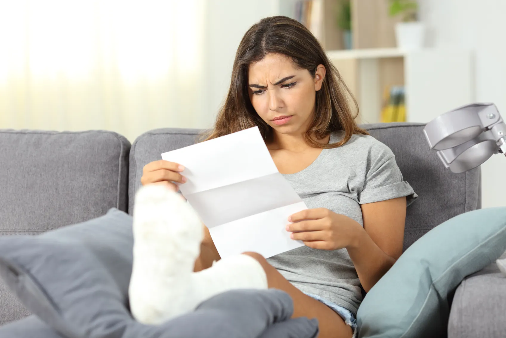 Women sitting on a couch, her leg in a cast, reading a letter.