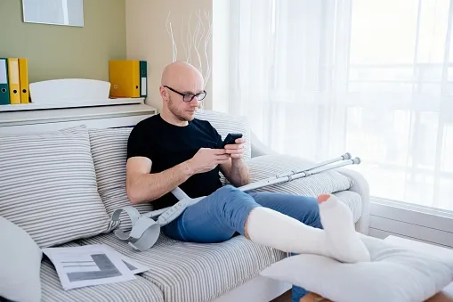 An injured person on his couch looking at his phone.