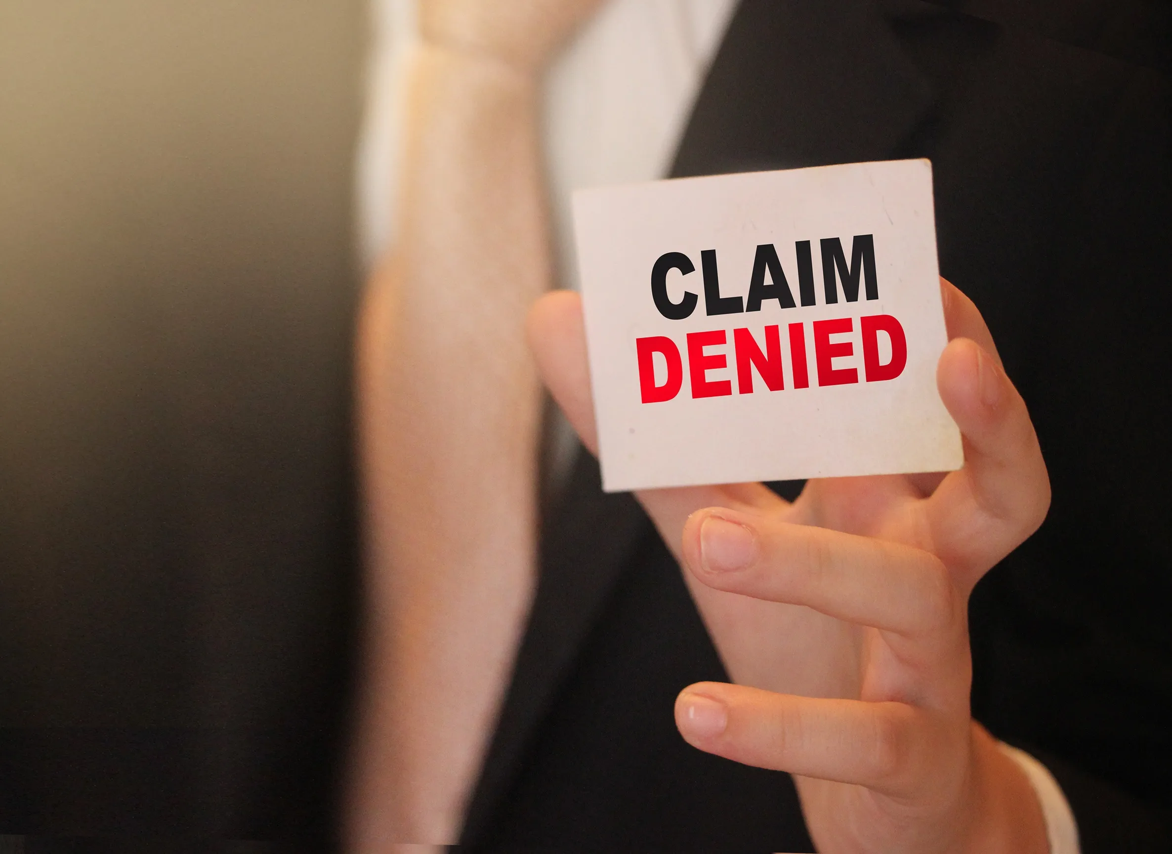 Person holding up a card that says: Claim Denied.
