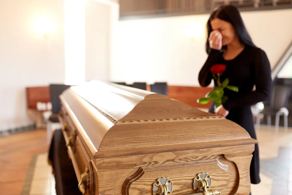 A woman holding a rose crying in front of a casket.