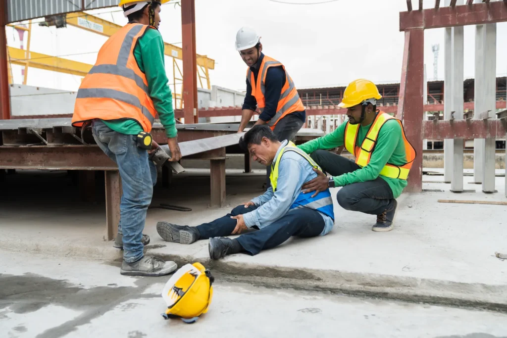 A construction worker holding his leg in pain while the other construction workers are helping him and moving what fell on him.