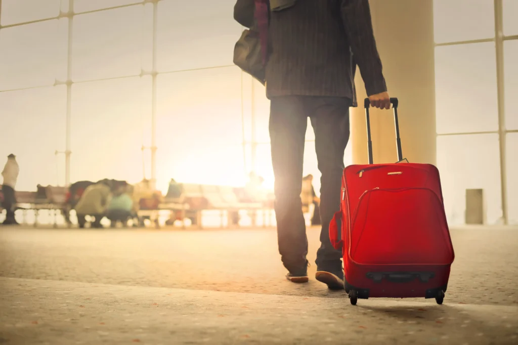 A man in a suit walking with a red suitcase.