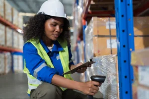 Female warehouse worker scanning barcodes on boxes stacked on shelves in a storage facility.