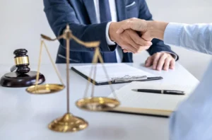 Handshake between two people in a legal office with gavel and scales of justice on the desk.