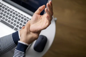 A person at a desk, hand on wrist, indicating a pain.